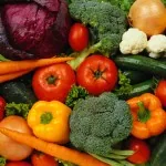 Colorful fresh vegetables including tomatoes, peppers, broccoli, carrots, mushrooms, beets and leafy greens arranged together