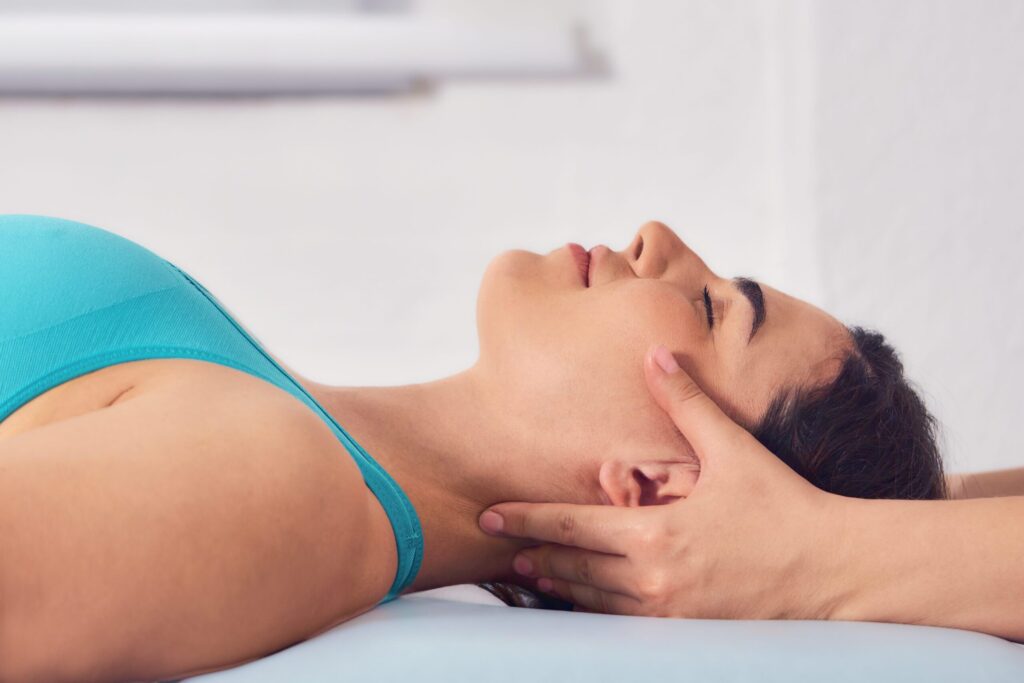 Woman lying on a treatment table receiving cranial chiropractic adjustment, practitioner's hands supporting her jaw and skull.